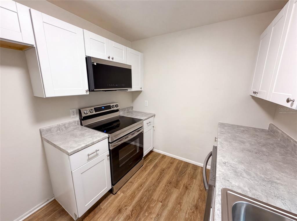 A kitchen features white cabinets, stainless steel appliances, and gray laminate countertops over wood flooring — 8310 ROLLING LOG DRIVE, ORLANDO, FL