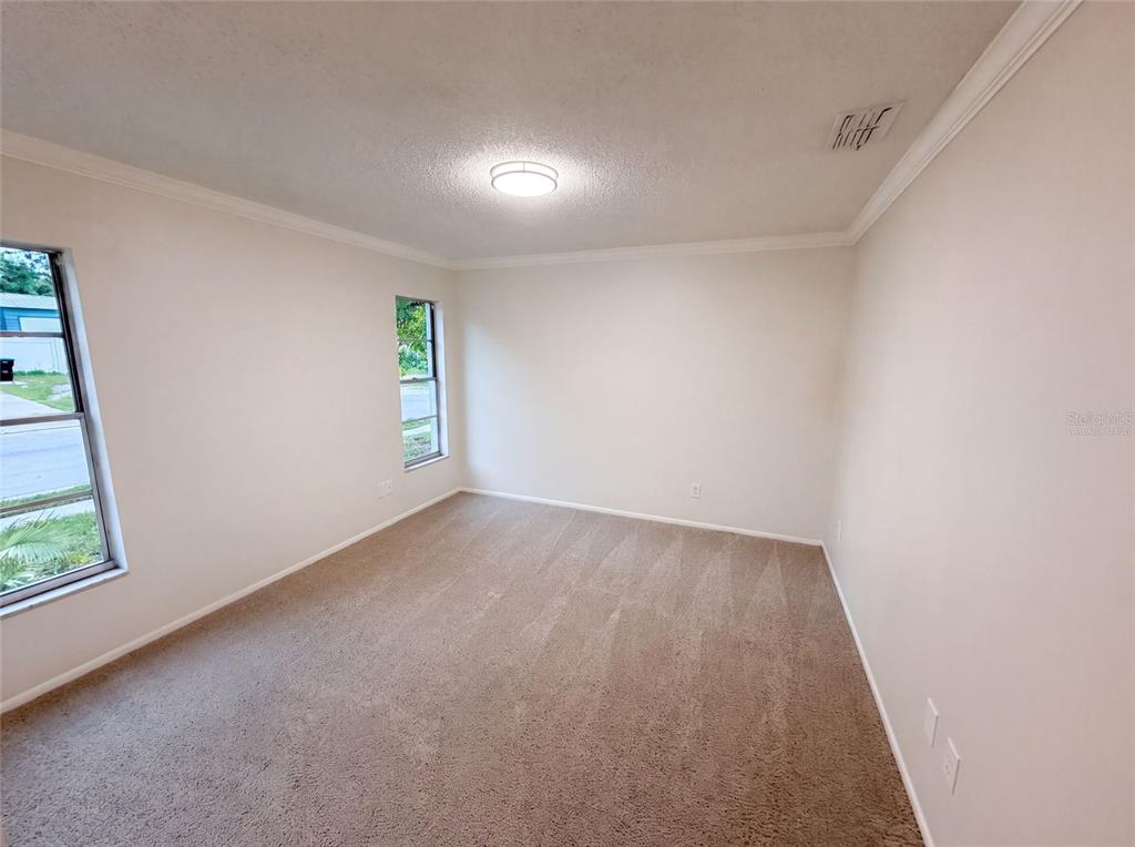 An empty bedroom features beige carpet, white walls, crown molding, and two windows — 8310 ROLLING LOG DRIVE, ORLANDO, FL