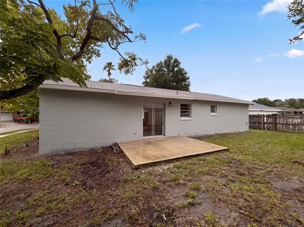 The exterior of a gray concrete block house features a sliding glass door and patio — 8310 ROLLING LOG DRIVE, ORLANDO, FL