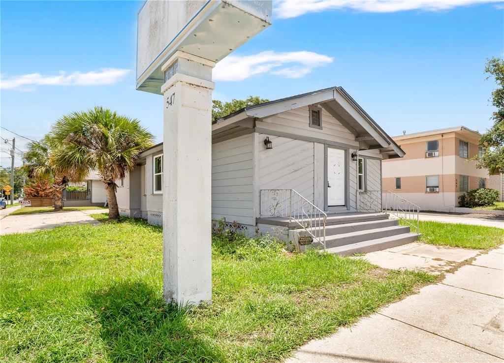 A small, light-gray house with a front porch and a prominent sign post in front — 547 N RIDGEWOOD AVENUE, DAYTONA BEACH, FL