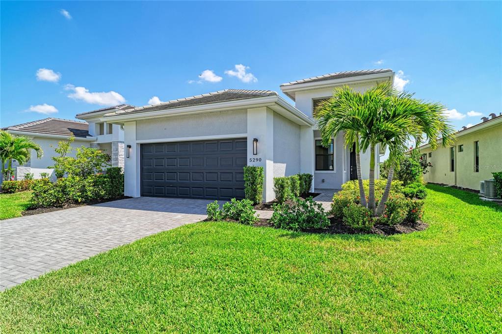 A single-story house with a gray garage door, a paved driveway, and a palm tree — 5290 BARNETT CIRCLE, BRADENTON, FL