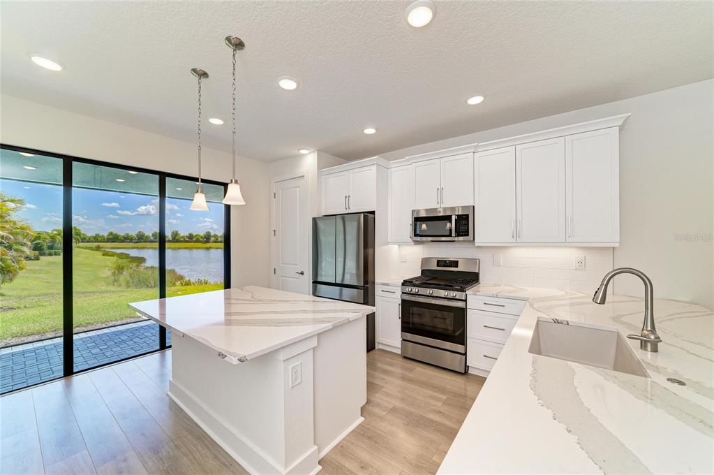 A modern kitchen features white cabinetry, quartz countertops, stainless steel appliances, and a water view — 5290 BARNETT CIRCLE, BRADENTON, FL