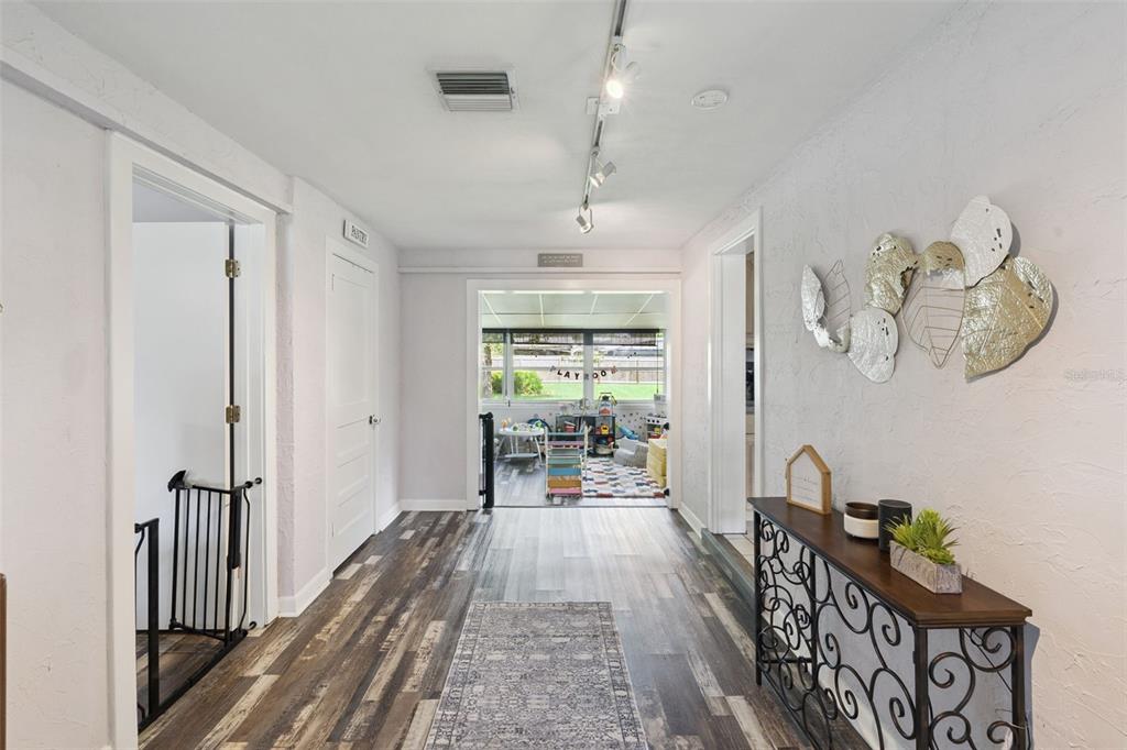 A hallway with wood-look flooring leads to a sunroom, featuring a console table and wall art — 106 ALANO ROAD, DEBARY, FL