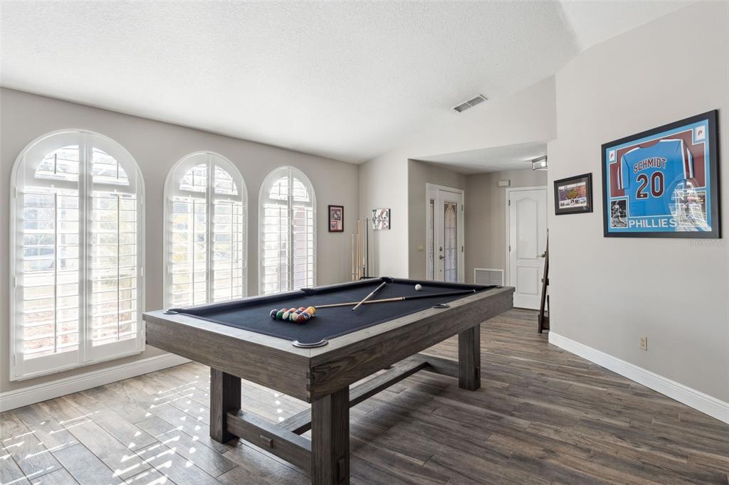 A game room features a pool table, wood-look tile flooring, and arched windows with shutters — 692 ROCHESTER STREET, OVIEDO, FL
