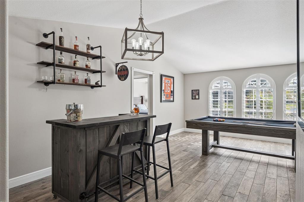 A game room features a wooden bar, industrial shelving, and a pool table near arched windows — 692 ROCHESTER STREET, OVIEDO, FL
