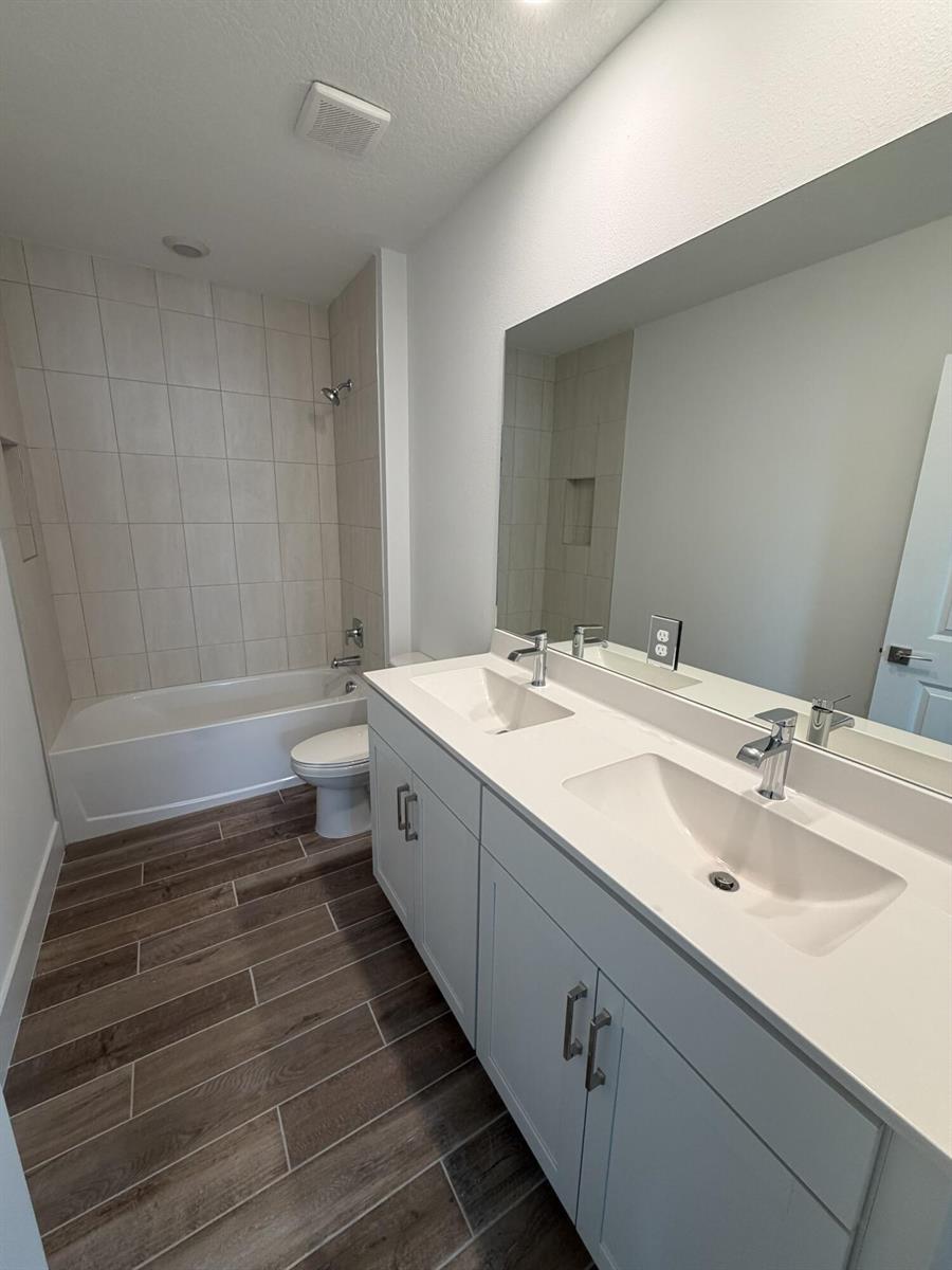 A bathroom features a double vanity with white cabinets, a tub-shower combo, and wood-look flooring — 6781 SE Park Trace Drive, Stuart FL 34997, STUART, FL