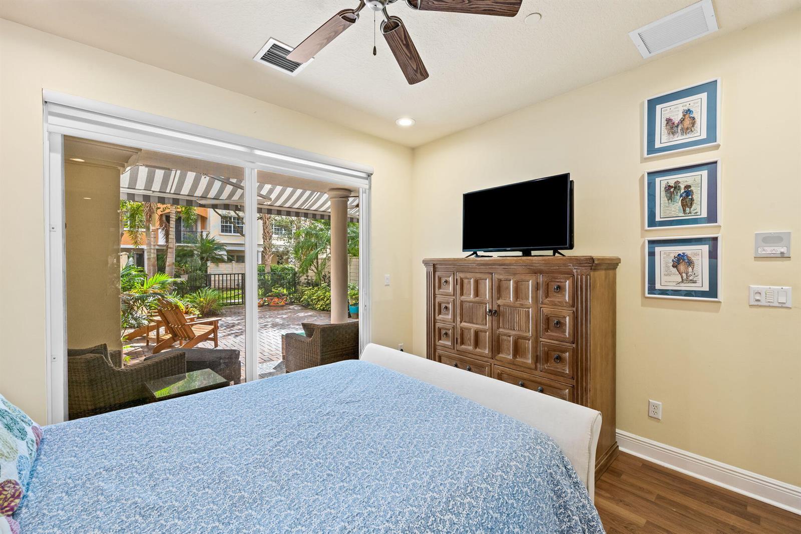 A bedroom with a bed, wooden dresser, television, and sliding glass doors leading to a patio — 5580 NE Trieste Terrace, Boca Raton FL 33487, BOCA RATON, FL