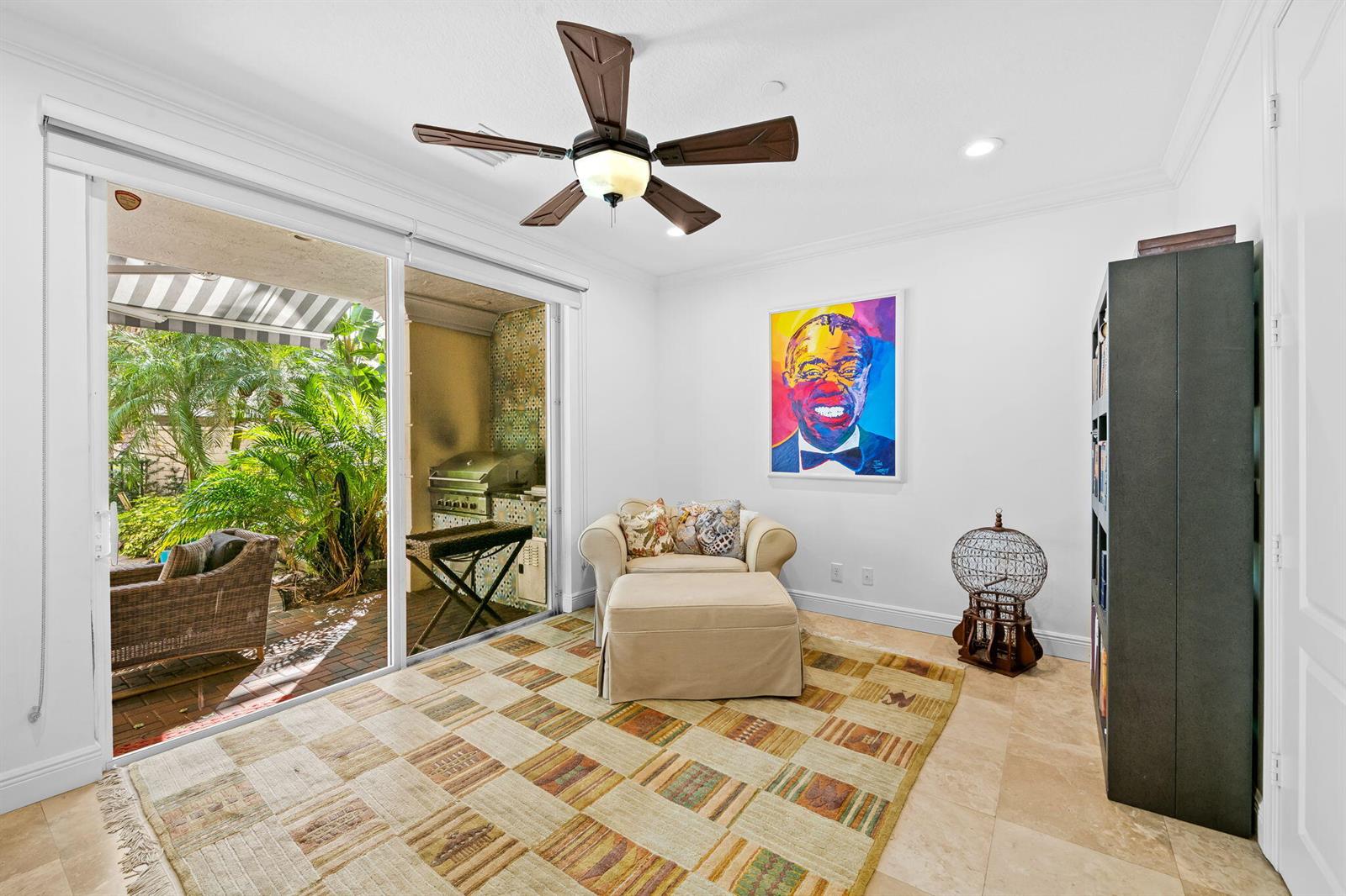 A sunroom features a beige armchair, a colorful portrait, a patterned rug, and sliding glass doors — 5580 NE Trieste Terrace, Boca Raton FL 33487, BOCA RATON, FL
