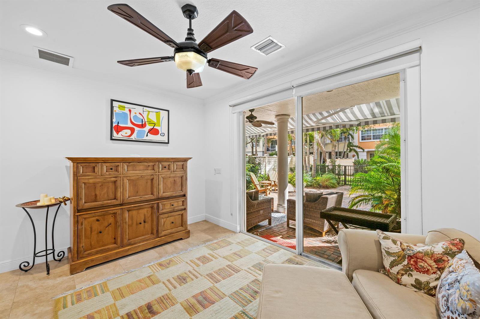 A living room with a wooden cabinet, ceiling fan, and sliding doors opening to a patio — 5580 NE Trieste Terrace, Boca Raton FL 33487, BOCA RATON, FL