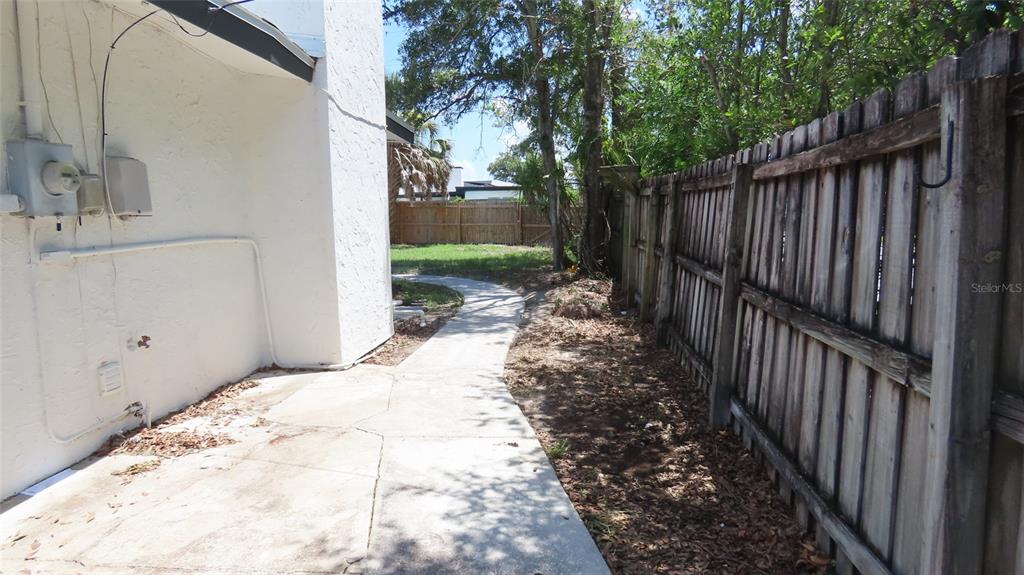 A concrete walkway leads along the side of a white house next to a wooden fence — 4594 17TH AVENUE N, ST PETERSBURG, FL