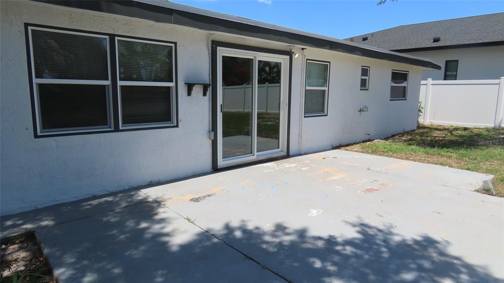 A concrete patio sits outside the back of a white house with sliding glass doors — 4594 17TH AVENUE N, ST PETERSBURG, FL