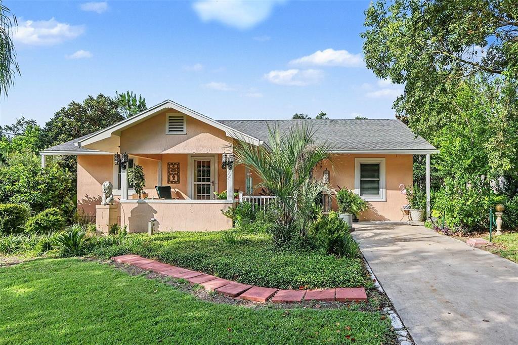 A single-story peach-colored house with a front porch, concrete driveway, and landscaped yard — 7480 E HIGHWAY 25, BELLEVIEW, FL