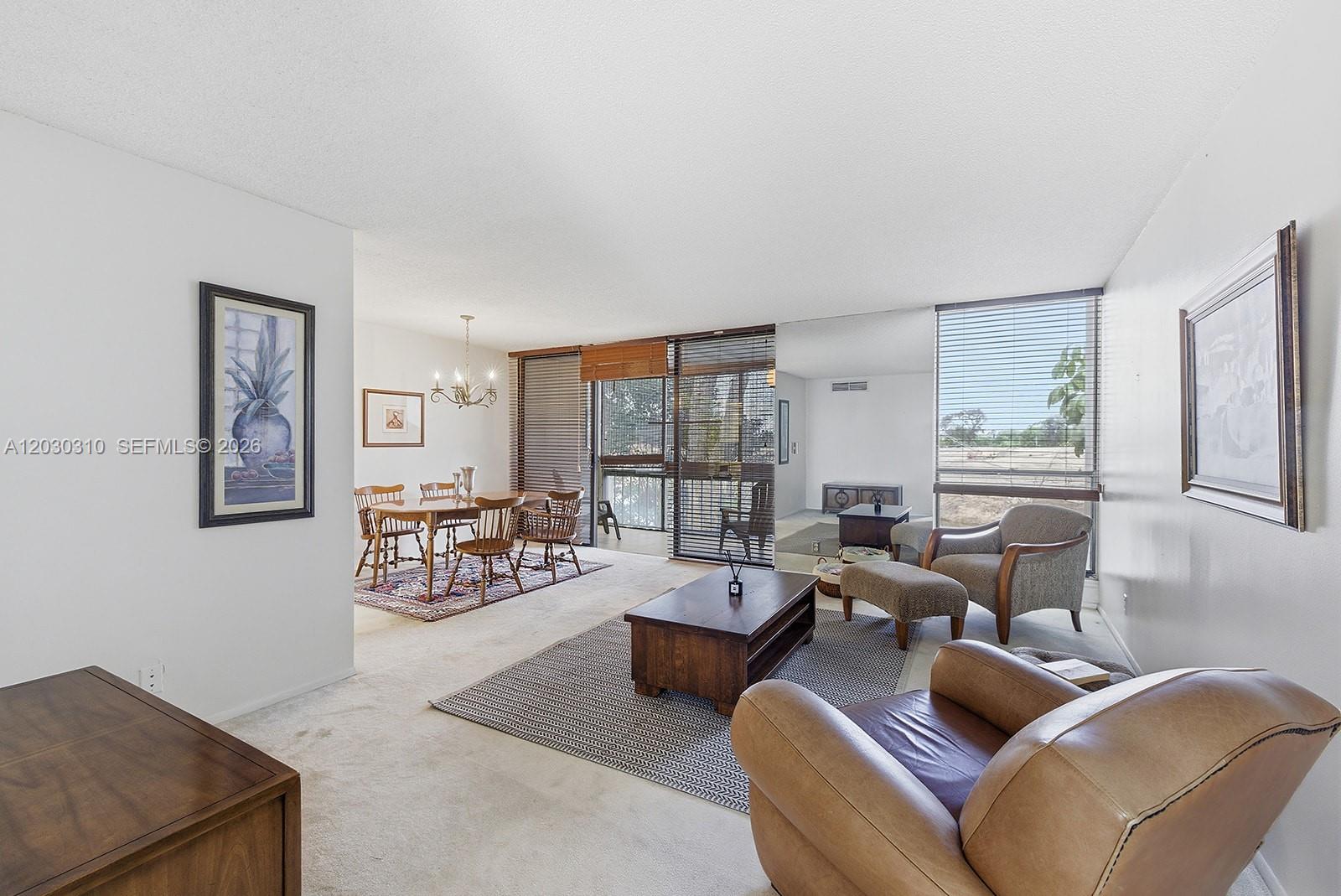 A living and dining room area features carpeted floors, large windows, and a sliding door — 1309 Bridgewood Dr, Boca Raton FL 33434, BOCA RATON, FL