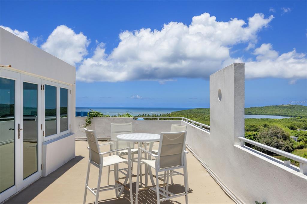 A white rooftop terrace features a dining set overlooking a coastal landscape and ocean — 200 OCEAN CLUB AT SEVEN SEAS UNIT DC-402, FAJARDO, PR