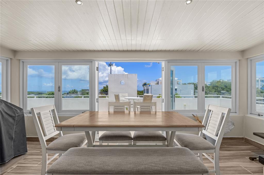 A dining room with a wooden table, chairs, and a bench, opening onto a sunny balcony — 200 OCEAN CLUB AT SEVEN SEAS UNIT DC-402, FAJARDO, PR