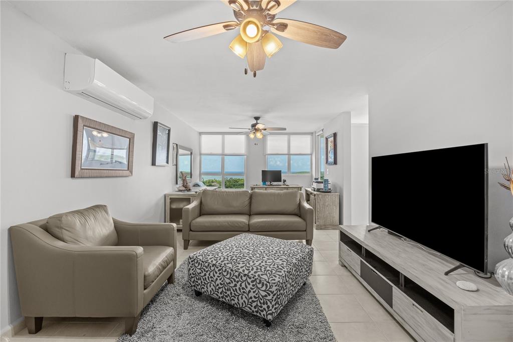 A living room features a leather sofa, armchair, patterned ottoman, and a large television — 200 OCEAN CLUB AT SEVEN SEAS UNIT DC-402, FAJARDO, PR