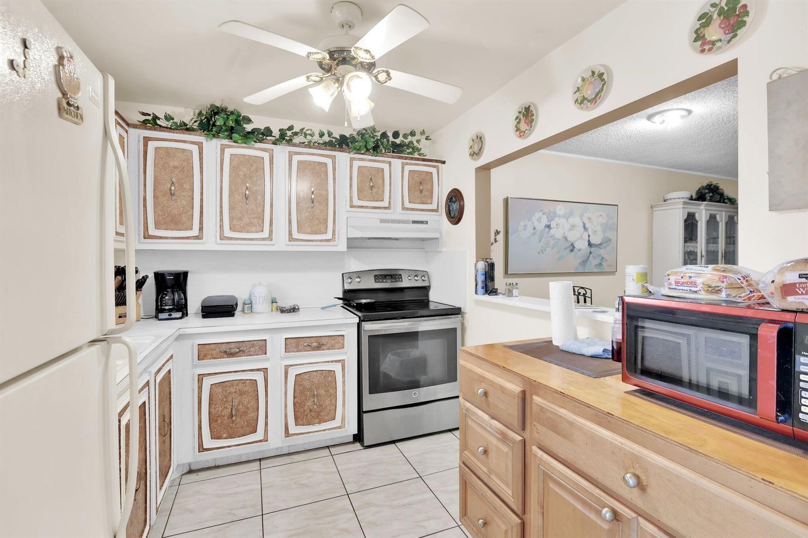 A kitchen features white cabinets with textured panels, stainless steel appliances, and a wooden island — 711 Lori Drive # 204, Palm Springs FL 33461, PALM SPRINGS, FL