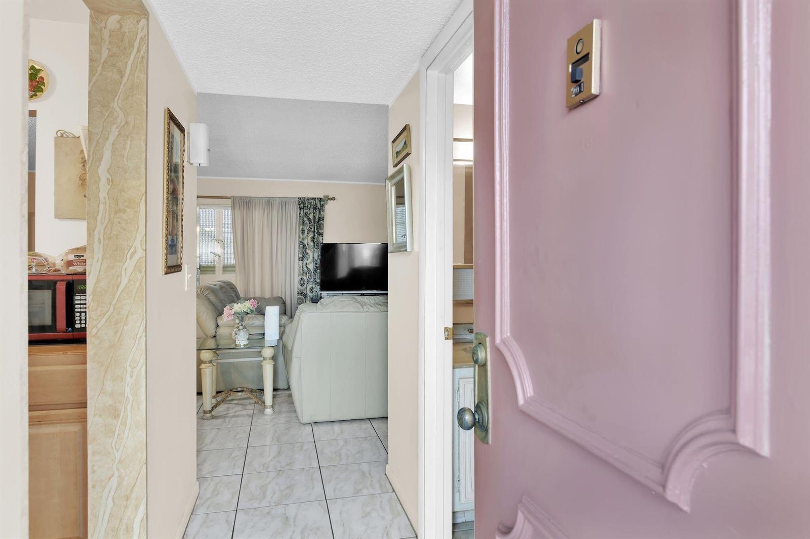A view from an open pink door into a living room with tiled floors — 711 Lori Drive # 204, Palm Springs FL 33461, PALM SPRINGS, FL