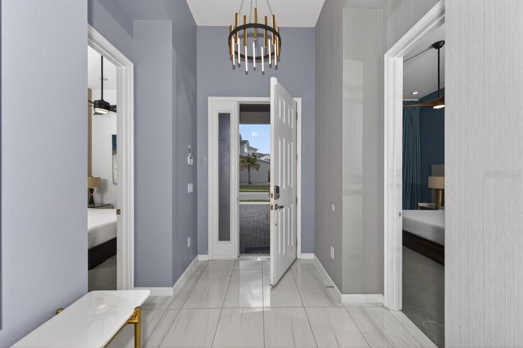 A bright entryway features a modern chandelier, white tiled floors, and doors to two bedrooms — 1735 OAK BLOSSOM DRIVE, DAVENPORT, FL