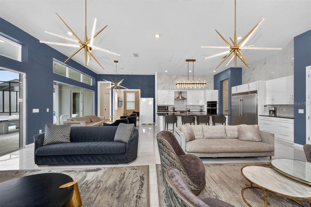 An open-concept living room and kitchen featuring blue accent walls, modern chandeliers, and tile flooring — 1735 OAK BLOSSOM DRIVE, DAVENPORT, FL