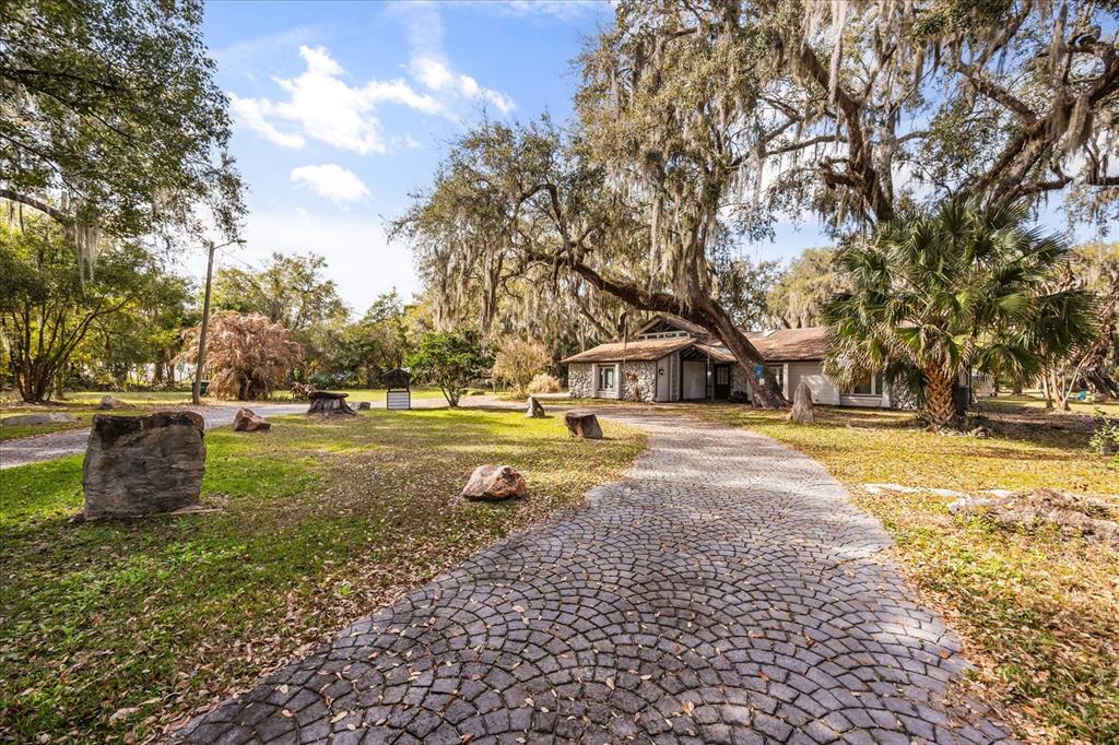 A stone-paved driveway leads to a house with a stone facade under large oak trees — 1775 HARBOR ROAD, KISSIMMEE, FL