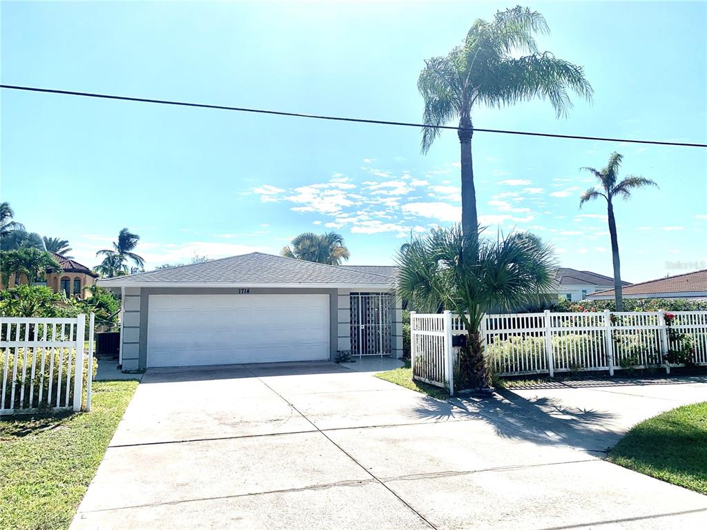 A single-story house with a white garage door, a gated entrance, and palm trees — 1714 MEADOWOOD STREET, SARASOTA, FL