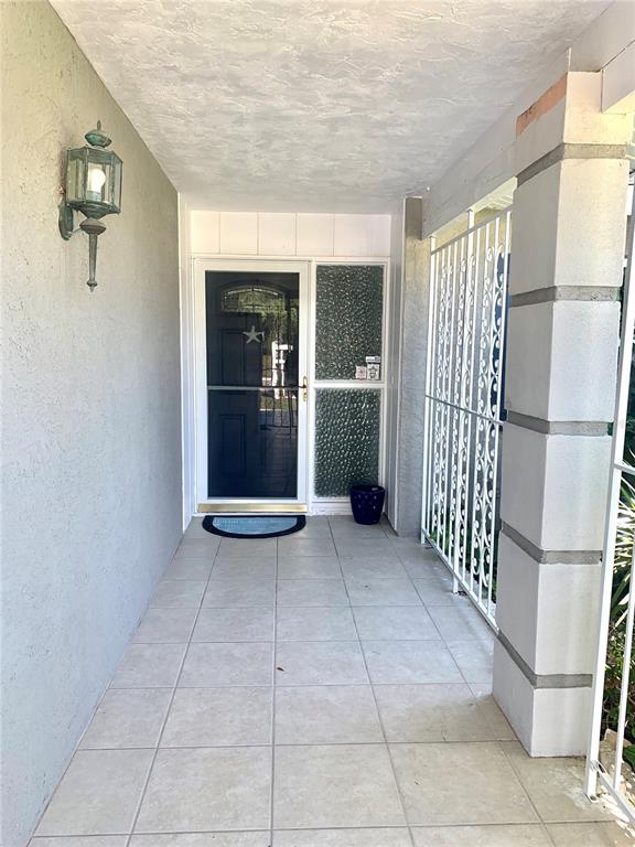 A covered entryway features tiled flooring, a glass-paneled door, and a decorative metal security gate — 1714 MEADOWOOD STREET, SARASOTA, FL