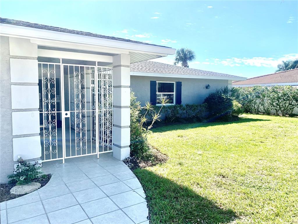 A white metal security gate stands at the entrance of a house with a tiled walkway — 1714 MEADOWOOD STREET, SARASOTA, FL