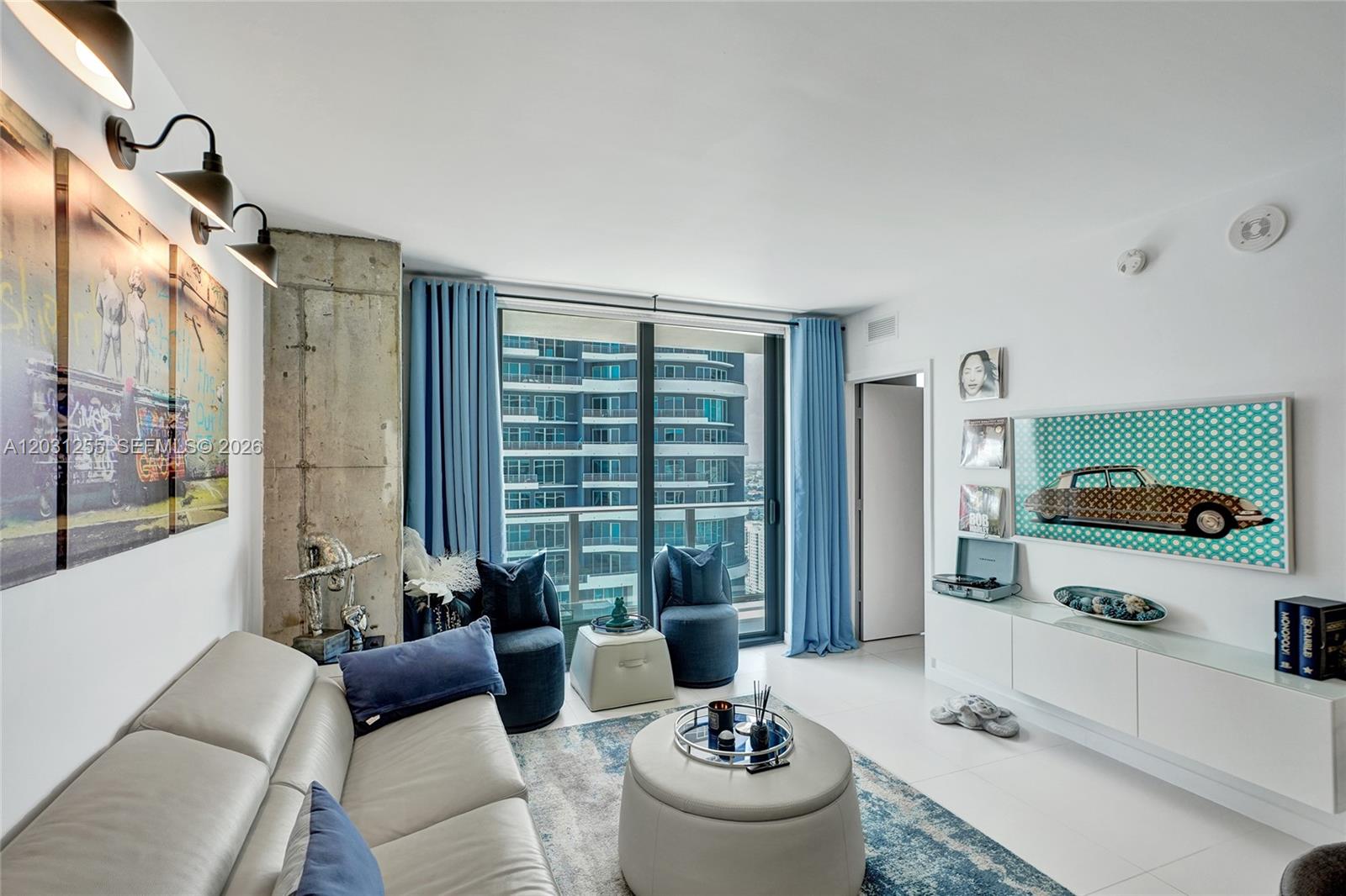 A modern living room features a grey sofa, blue curtains, and a view of buildings — 1300 S Miami Ave # 4508, Miami FL 33130, MIAMI, FL