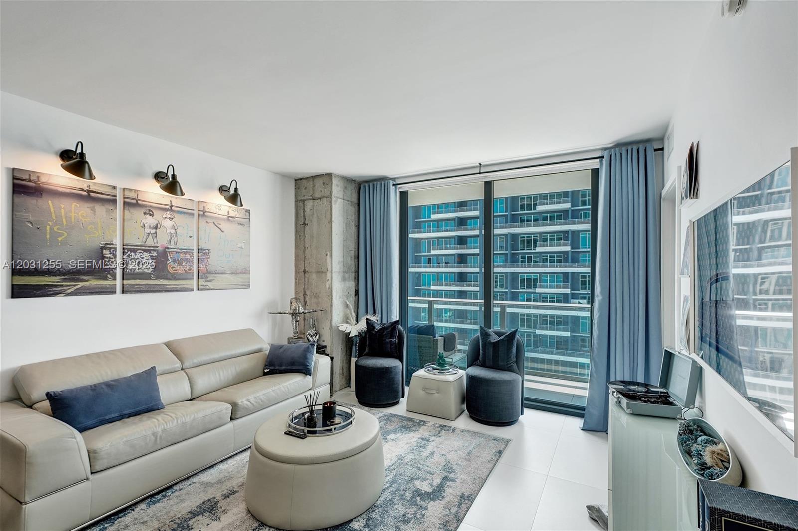 A modern living room features a beige sofa, a round ottoman, and floor-to-ceiling windows — 1300 S Miami Ave # 4508, Miami FL 33130, MIAMI, FL