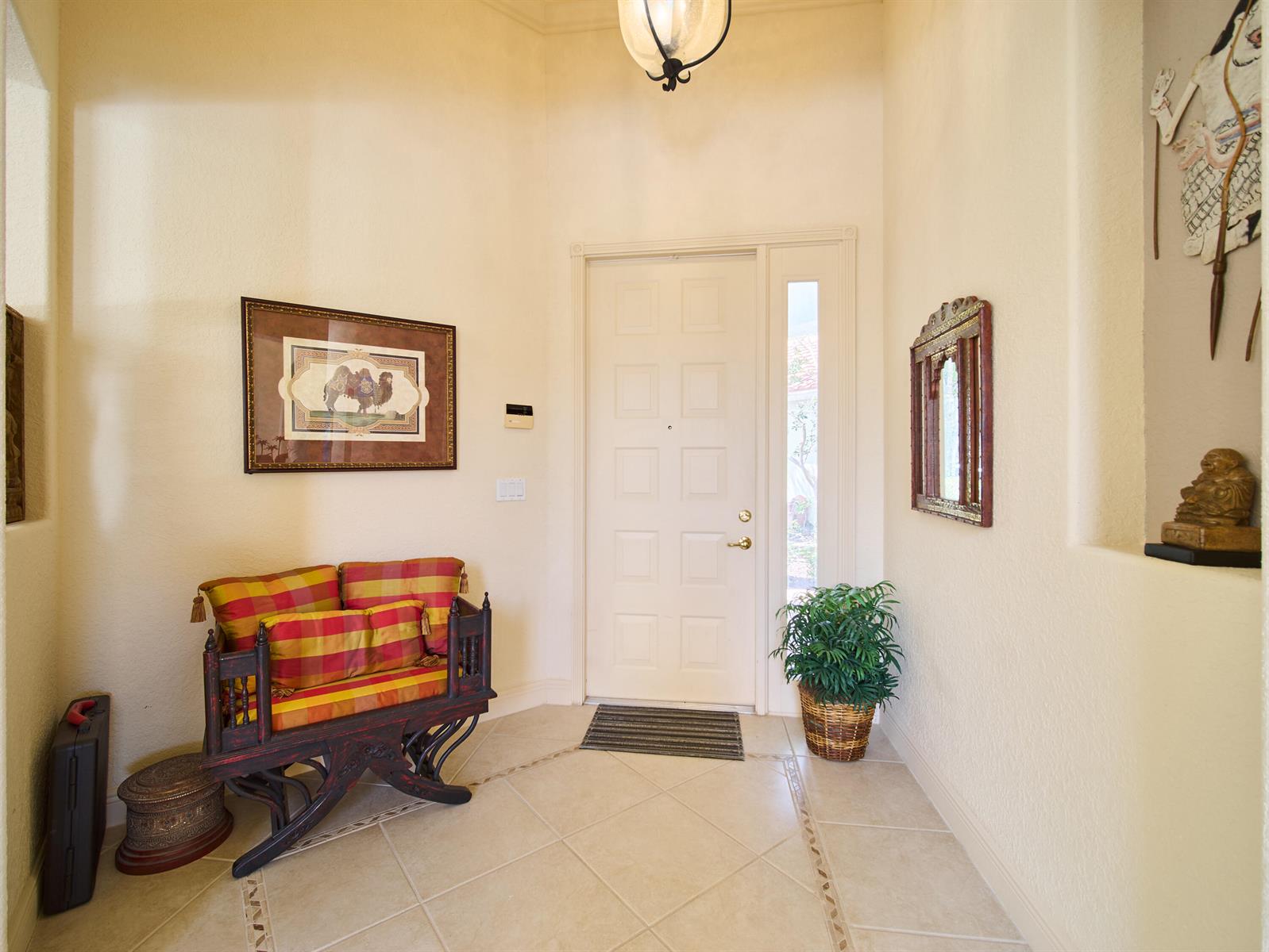 A bright entryway features tiled floors, a wooden bench with plaid cushions, and a front door — 8282 Spyglass Drive, West Palm Beach FL 33412, WEST PALM BEACH, FL