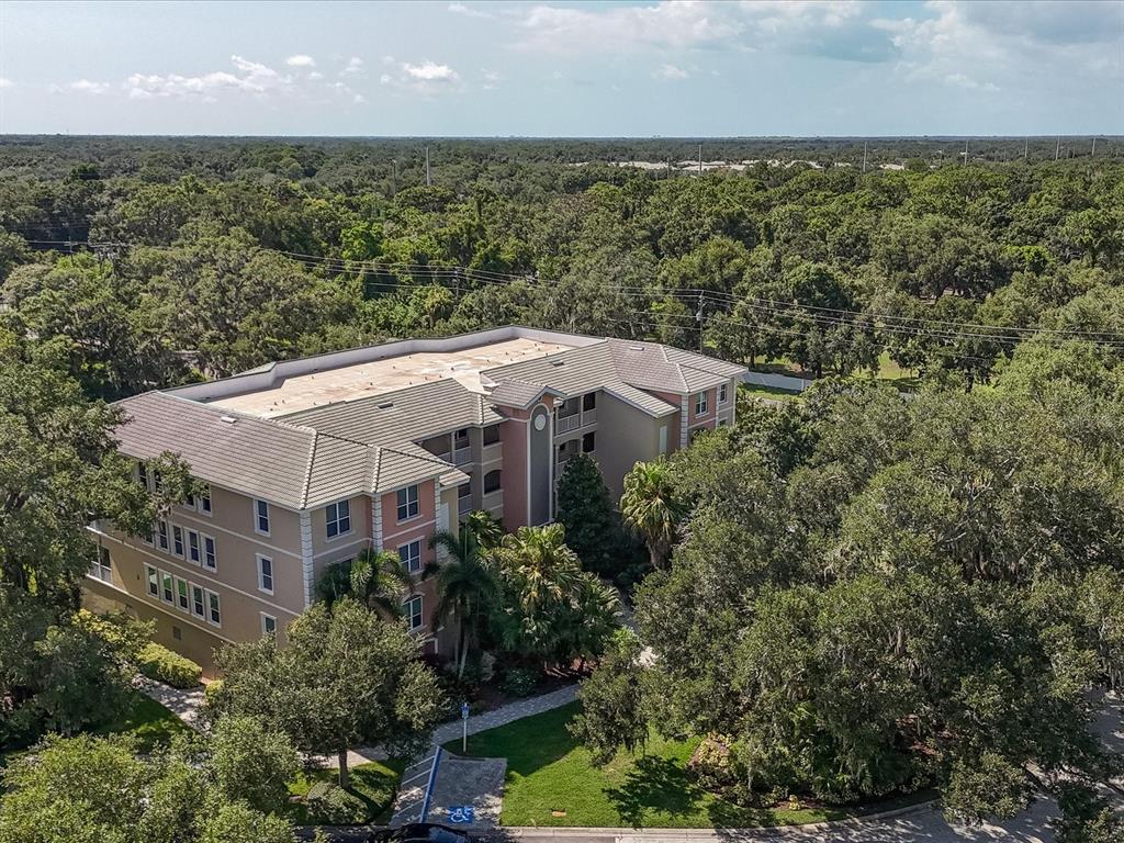 An aerial view shows a multi-story apartment building surrounded by dense trees and greenery — 5122 MANORWOOD DRIVE UNIT 4B, SARASOTA, FL