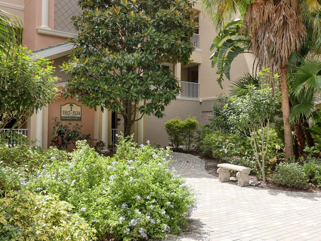 A paved walkway leads to the entrance of a multi-story building surrounded by lush landscaping — 5122 MANORWOOD DRIVE UNIT 4B, SARASOTA, FL