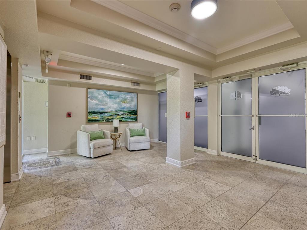 A tiled lobby features two armchairs, a small side table, and glass entry doors — 5122 MANORWOOD DRIVE UNIT 4B, SARASOTA, FL