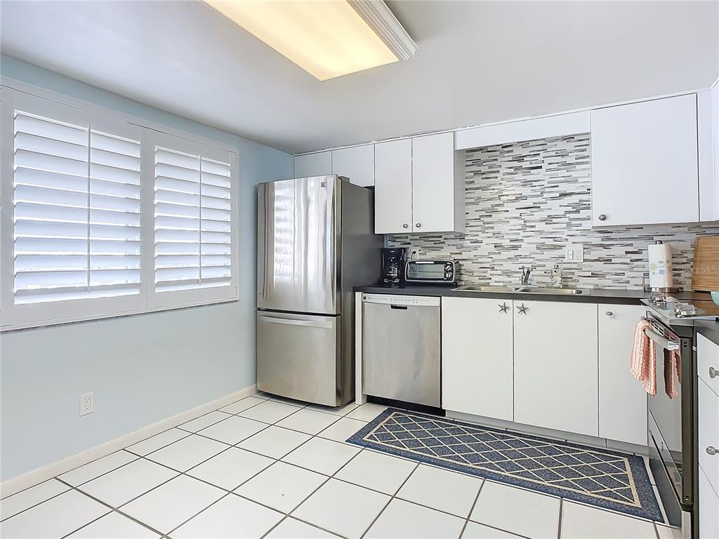 A kitchen features white cabinets, stainless steel appliances, a tiled backsplash, and white floor tiles — 3663 S ATLANTIC AVENUE UNIT 20C, NEW SMYRNA BEACH, FL
