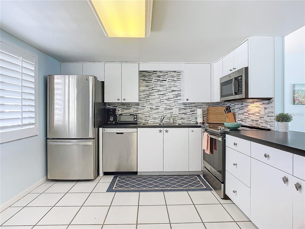 A kitchen with white cabinets, stainless steel appliances, a tiled backsplash, and white floor tiles — 3663 S ATLANTIC AVENUE UNIT 20C, NEW SMYRNA BEACH, FL