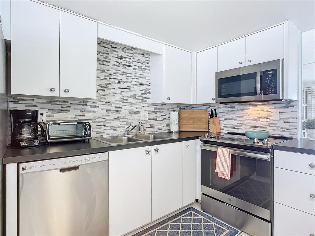 A kitchen features white cabinets, stainless steel appliances, a dark countertop, and a tiled backsplash — 3663 S ATLANTIC AVENUE UNIT 20C, NEW SMYRNA BEACH, FL