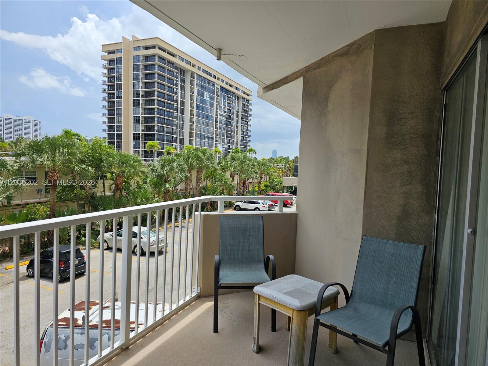 A balcony features two chairs, a small table, and a view of a parking lot — HALLANDALE BEACH, FL