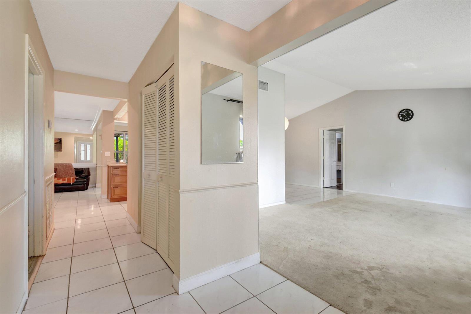 A hallway with white tile flooring leads to a living area with beige carpeting — 1197 Belmore Terrace, Wellington FL 33414, WELLINGTON, FL