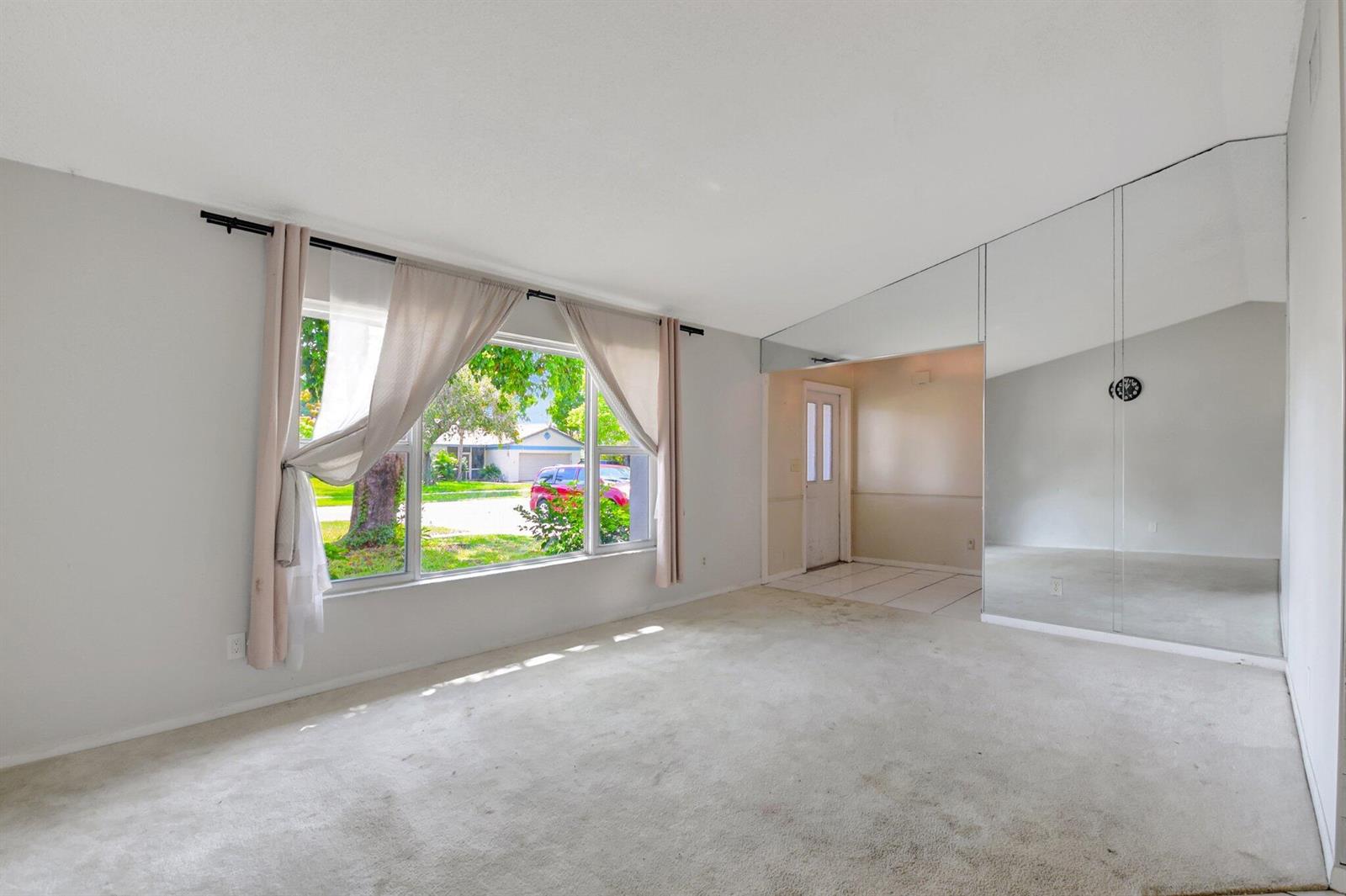 A living room with beige carpet, a large window, and a mirrored wall — 1197 Belmore Terrace, Wellington FL 33414, WELLINGTON, FL