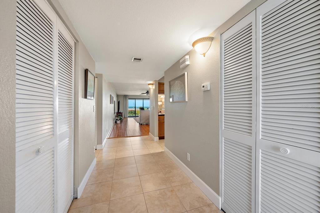 A tiled hallway leads past louvered closet doors toward a living area with ocean views — 4450 GULF BOULEVARD UNIT 110, ST PETE BEACH, FL