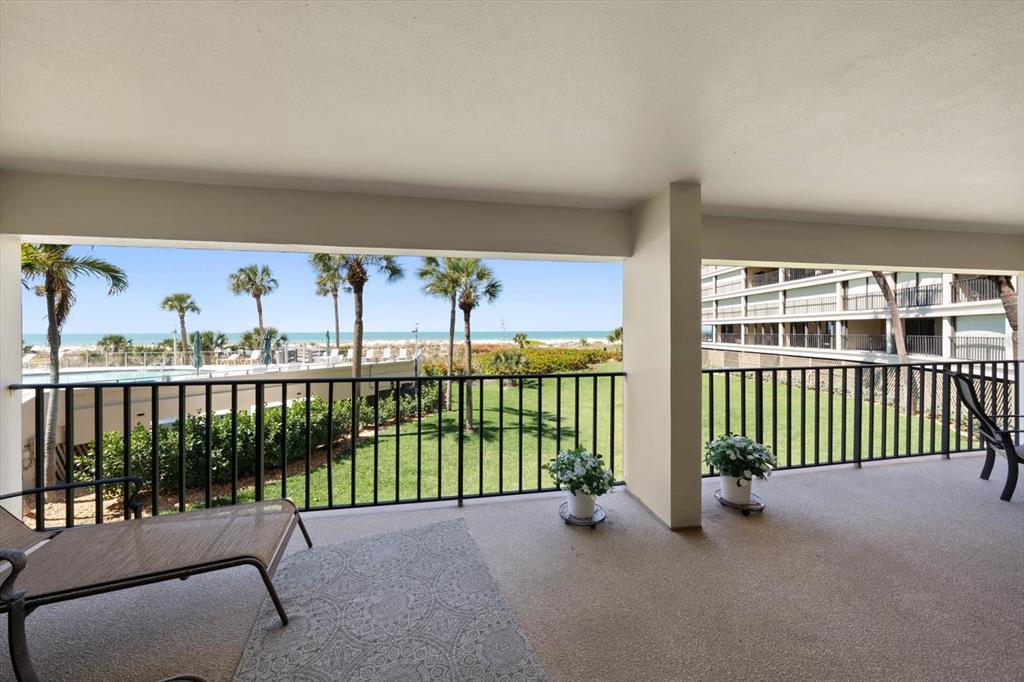 A covered balcony overlooks a grassy lawn, palm trees, and the ocean beyond — 4450 GULF BOULEVARD UNIT 110, ST PETE BEACH, FL