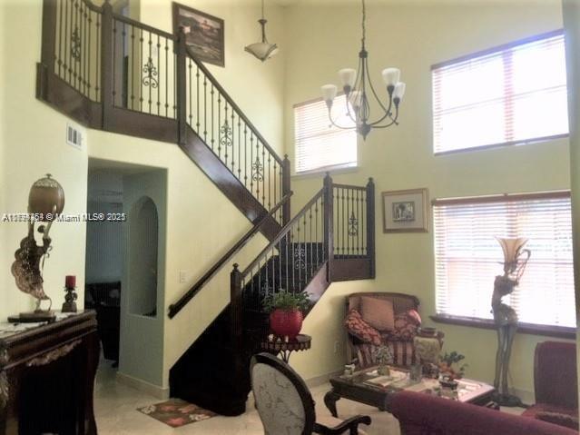 A living room features a wooden staircase with iron railings, a chandelier, and large windows — 4854 NW 110th Pl, Doral FL 33178, DORAL, FL