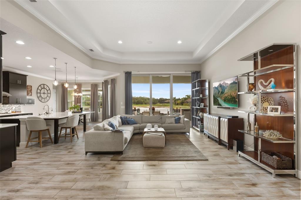 An open-concept living room and kitchen featuring light wood-look tile floors and a large sectional — 3967 EQUINE COVE, LAKE MARY, FL