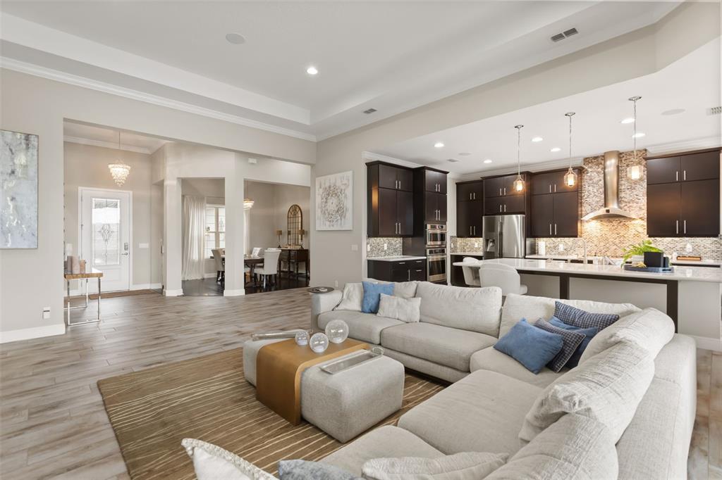 An open-concept living room and kitchen featuring dark cabinetry, light flooring, and a large sectional — 3967 EQUINE COVE, LAKE MARY, FL
