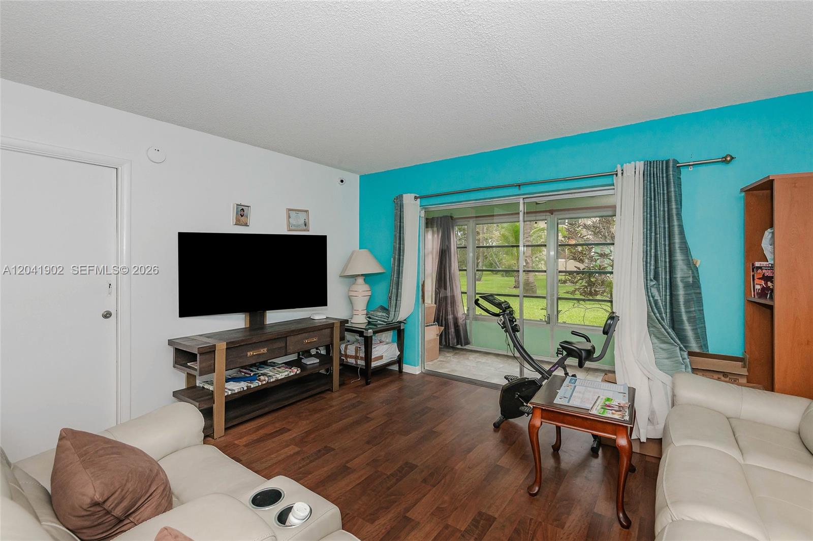 A living room features a television, exercise bike, and sliding glass doors to a patio — 7200 NW 4th Pl # 101, Margate FL 33063, MARGATE, FL