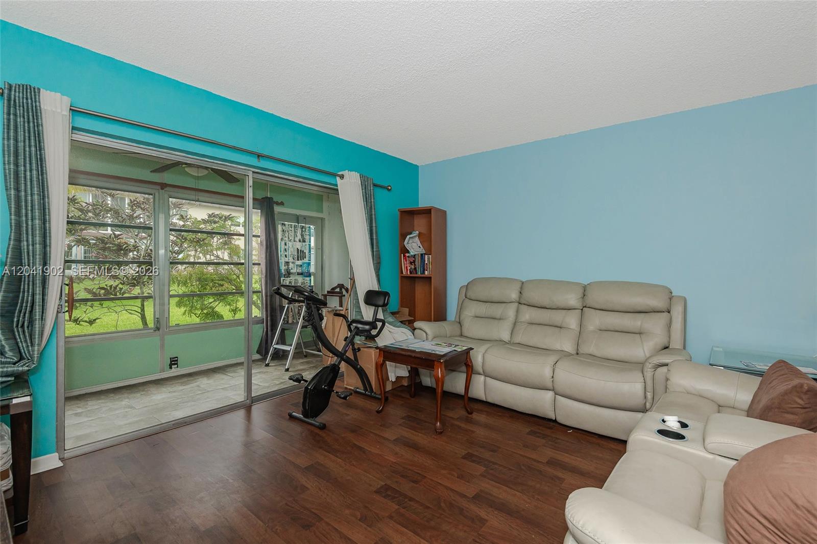 A living room features light blue walls, wood-look flooring, a leather sofa, and a sliding door — 7200 NW 4th Pl # 101, Margate FL 33063, MARGATE, FL