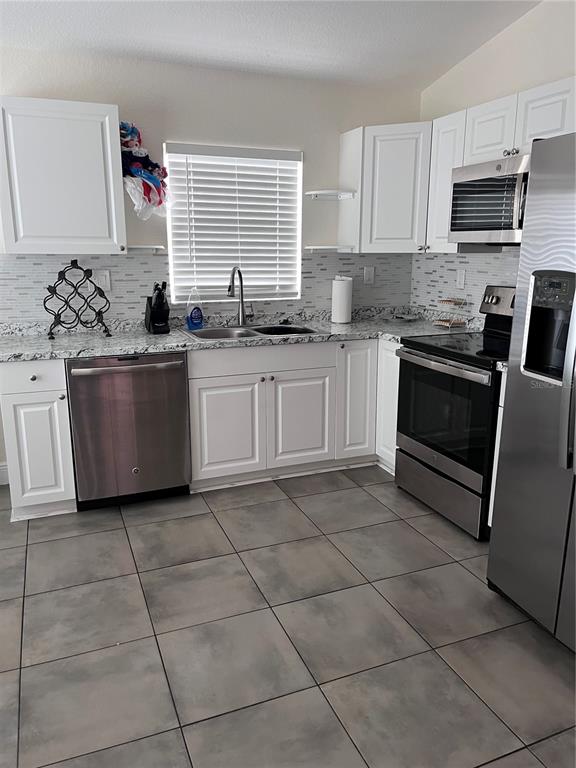 A kitchen features white cabinets, stainless steel appliances, granite countertops, and gray tiled flooring — 2127 W PERIO STREET UNIT 1, TAMPA, FL