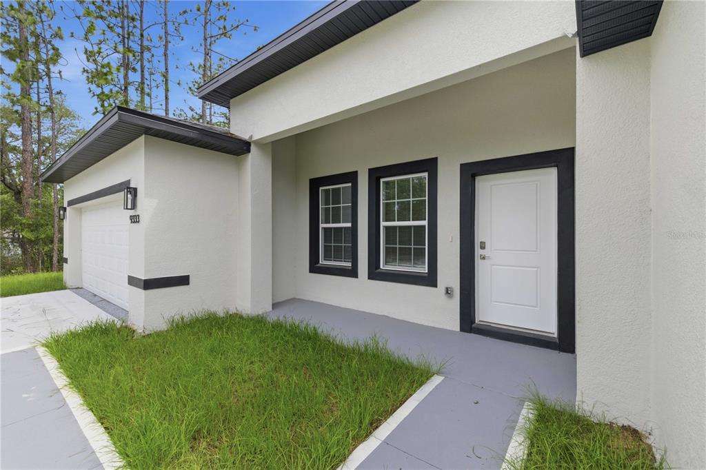 A white house exterior features a garage, a front door, and two windows with black trim — 9333 N SAMOA WAY, CITRUS SPRINGS, FL