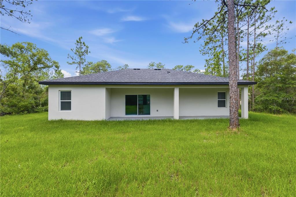 The rear exterior of a single-story house features a covered patio and a grassy yard — 9333 N SAMOA WAY, CITRUS SPRINGS, FL